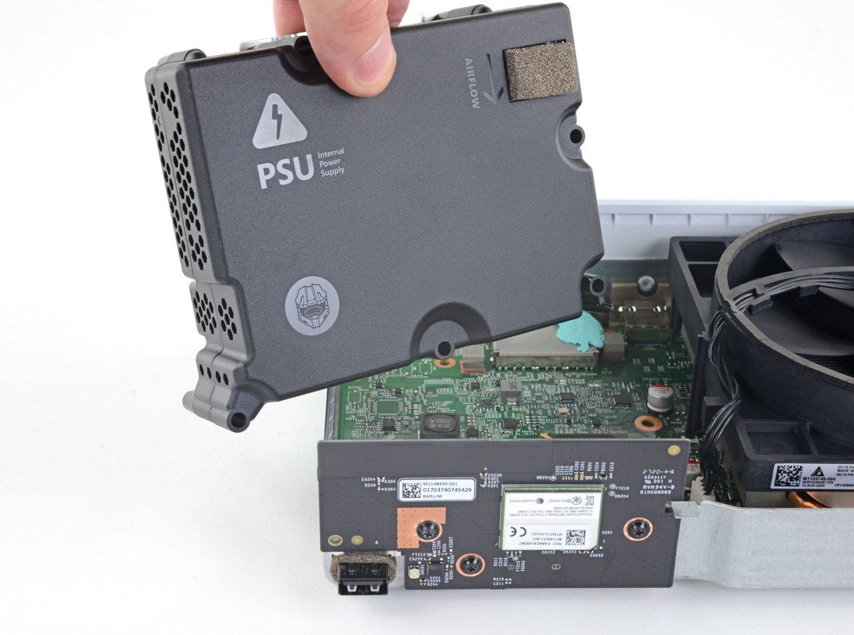A person holding a power supply unit for an Xbox Series S, with the system's internal components visible in the background.