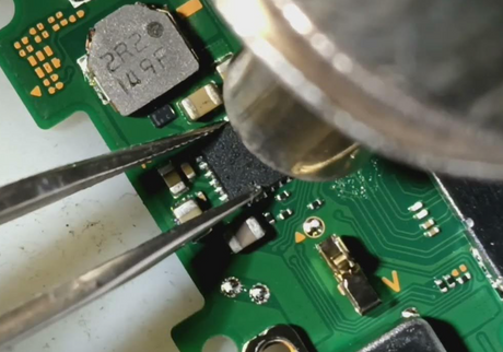 Close-up of a circuit board with tweezers and a magnifying glass.